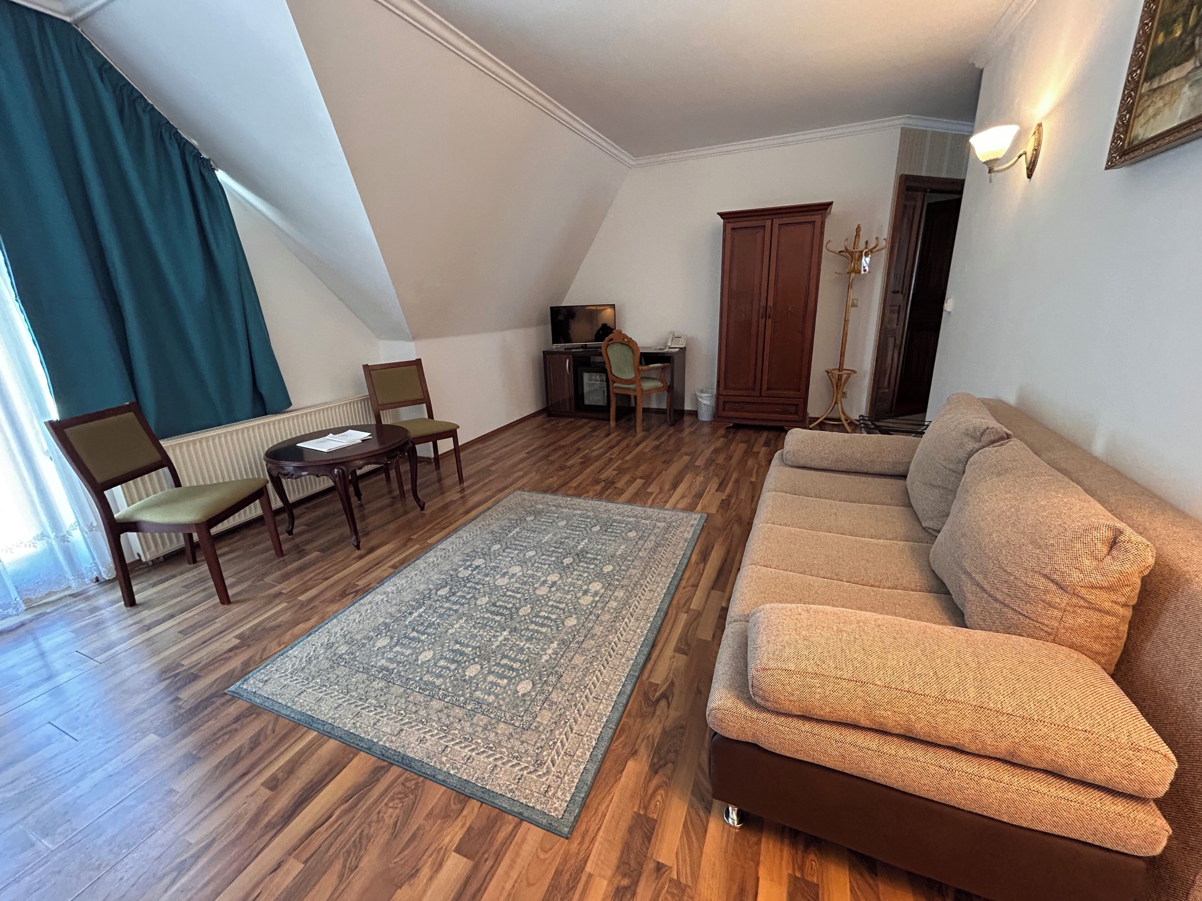 A living room with a sofa, chairs, a coffee table, a rug, a radiator, a television, and a cabinet.