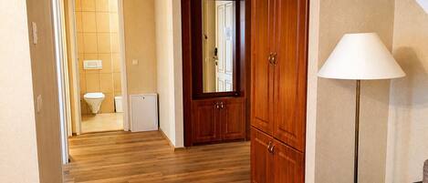 A hallway with wooden flooring, a black sofa, a lamp, and a wooden wardrobe.