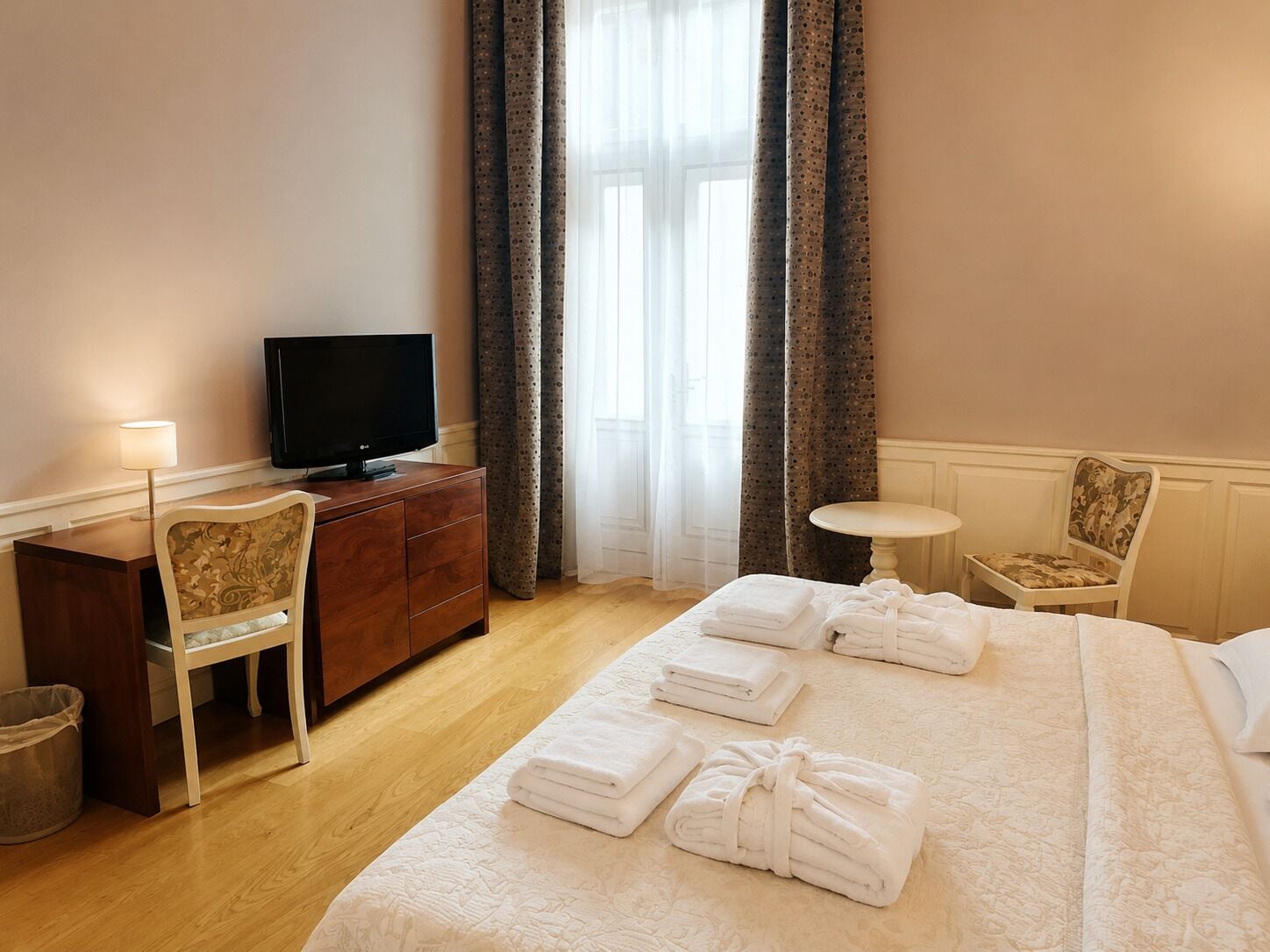 A hotel room with a bed, a TV, a desk, a chair, and a small table.