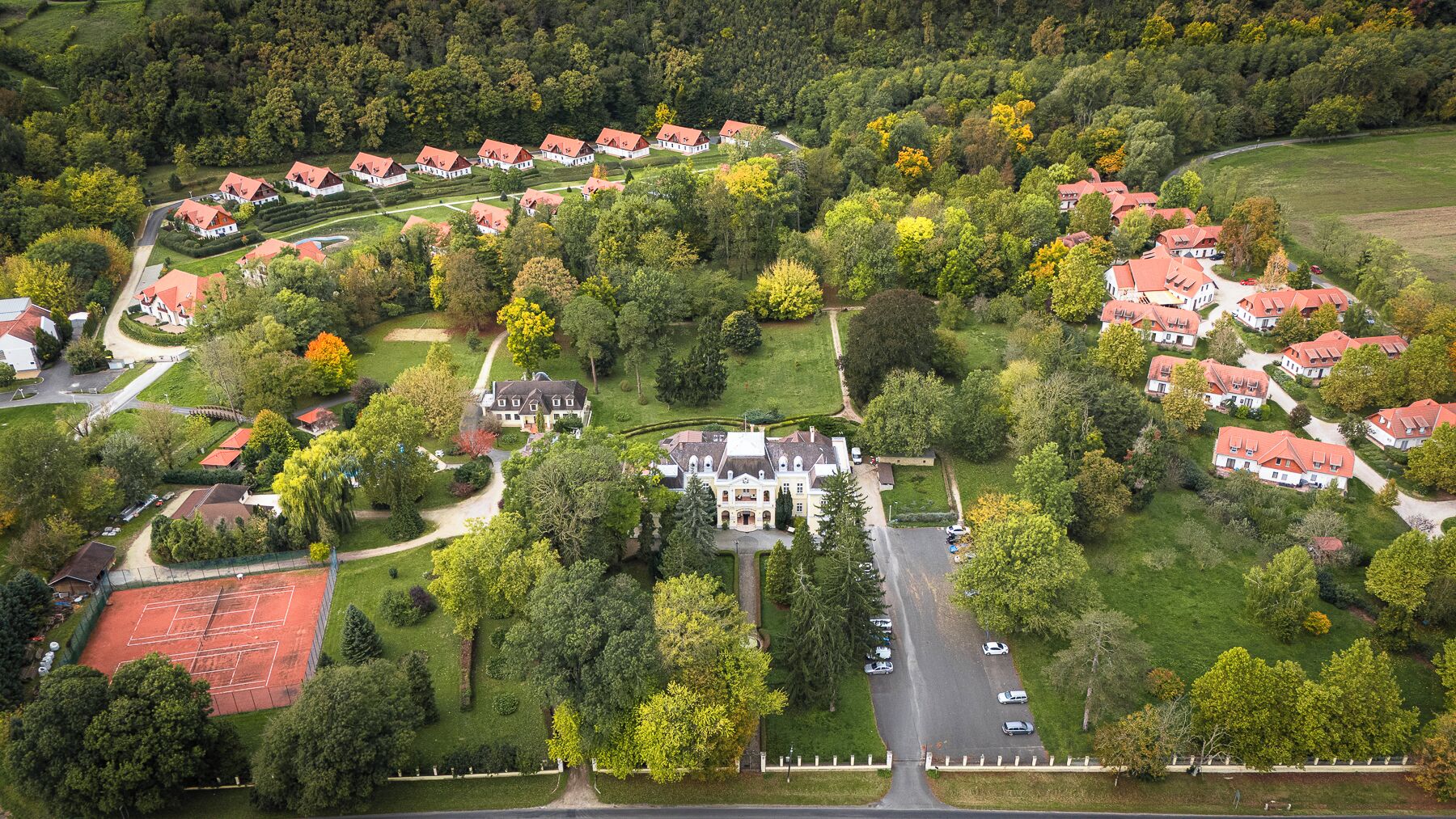 Vue aérienne d’un quartier résidentiel avec des maisons, un grand bâtiment central et de nombreux espaces verts environnants.
