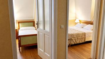 A hotel room with a wooden floor, a bed with a patterned bedspread, a bedside table with a lamp, and a window with blinds.