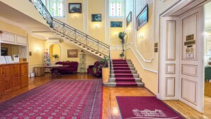 A grand foyer with a staircase, a reception desk, and a seating area. - Batthyány Kastélyszálló (Zalacsany)