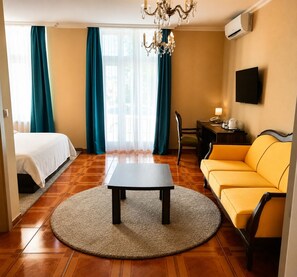 Habitación de hotel con cama, sofá, mesa, silla, escritorio y televisor.