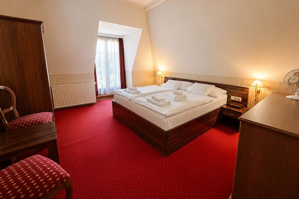 A hotel room with a large bed, a desk, a chair, and a radiator.