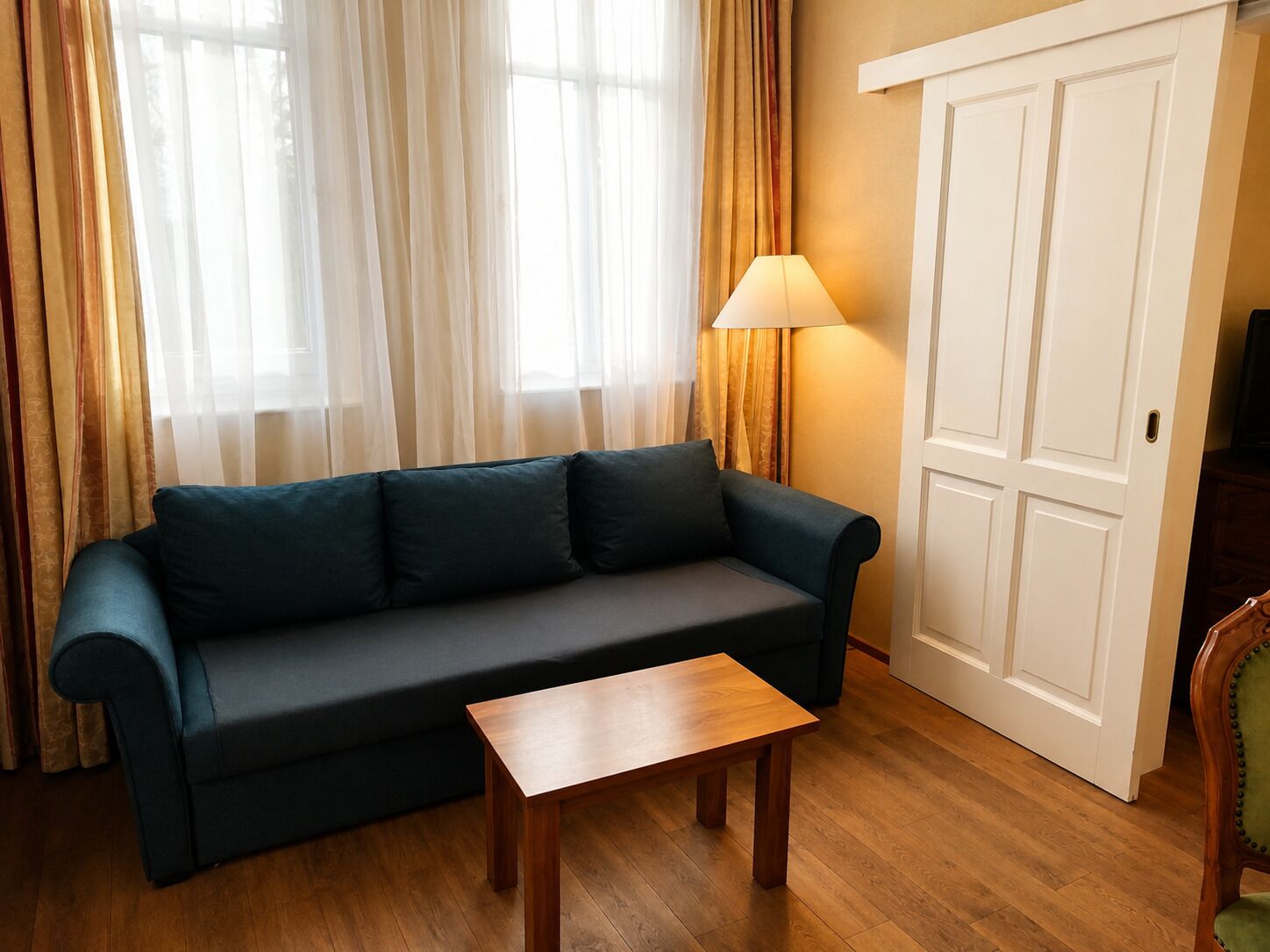 A living room with a dark green sofa, a wooden coffee table, a lamp, and a door.