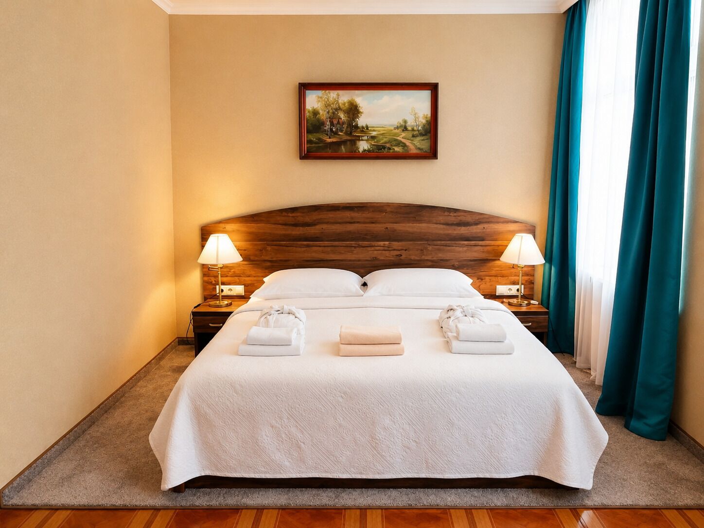 Una cama bien hecha con sábanas blancas, dos lámparas de noche, un cuadro en la pared y una ventana con cortinas.