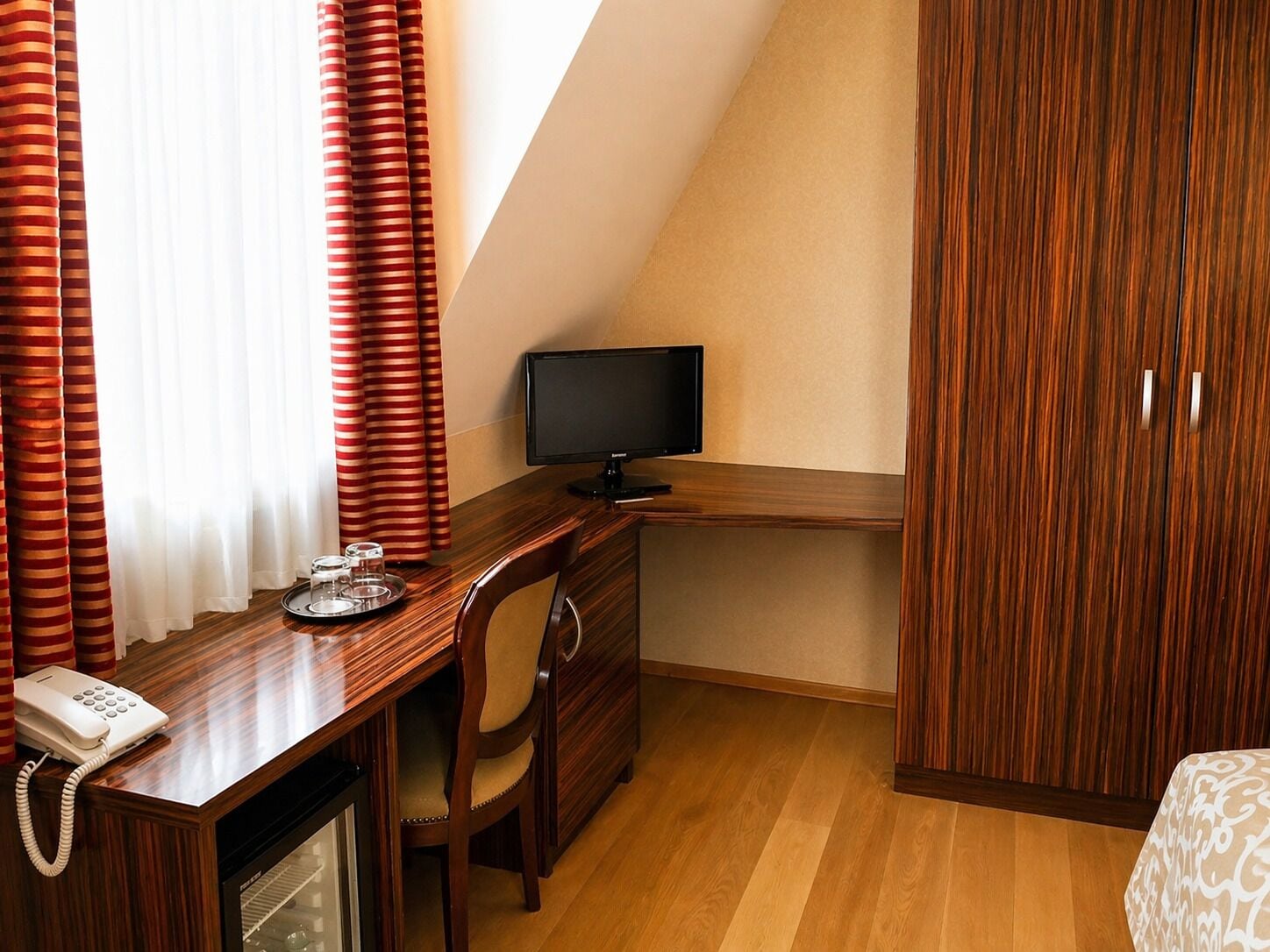 Habitación de hotel con escritorio de madera, televisor, teléfono, silla y armario.