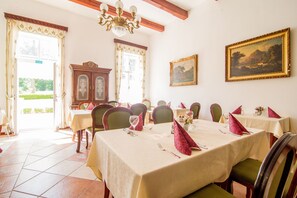 Un comedor con mesas dispuestas para una comida, sillas, una araña y un cuadro en la pared.
