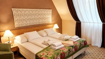 Una habitación de hotel con una cama, dos lámparas de noche, una colcha con motivos florales, un tapiz estampado y una ventana con cortinas.