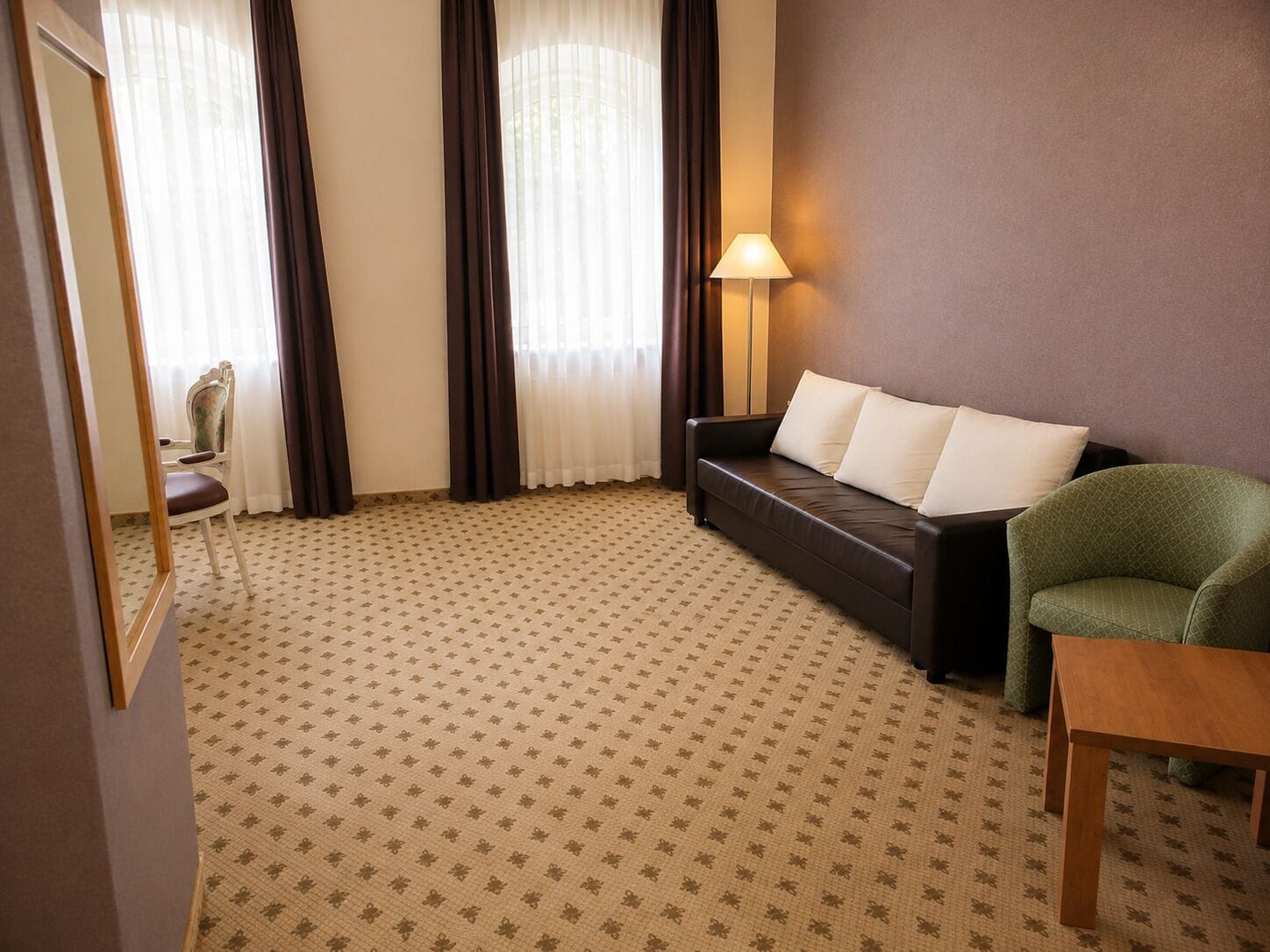Una habitación con alfombra estampada, un sofá con cojines, una silla, una lámpara y una mesa.