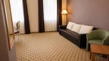 Una habitación con alfombra estampada, un sofá con cojines, una silla, una lámpara y una mesa.