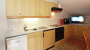 A kitchen with wooden cabinets, a dishwasher, a coffee machine, and a television. - Quaint Apartment in Finkenberg near Ski Lift (Finkenberg)