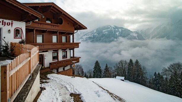 A traditional wooden chalet with a balcony, set against a backdrop of snow-covered mountains and clouds. - Quaint Apartment in Finkenberg near Ski Lift (Finkenberg)