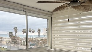 A dining area with a table, chairs, a ceiling fan, a window with blinds, and a view of the beach. - Sea view apartment in SETE (Sète)