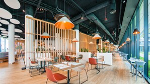 A modern restaurant with wooden flooring, white and orange pendant lights, and a variety of seating arrangements including tables and chairs. - Apartamenty Sun & Snow Seaside Kołobrzeg (Kolobrzeg)