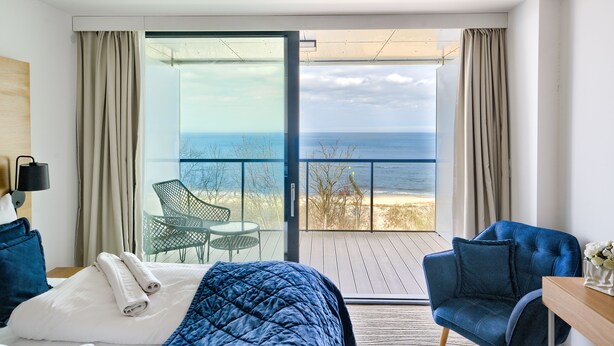 A hotel room with a large sliding glass door leading to a balcony with a view of the beach and ocean. - Apartamenty Sun & Snow Seaside Kołobrzeg (Kolobrzeg)