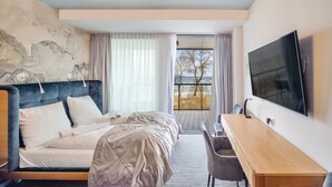 A hotel room with a bed, a desk, a TV, and a balcony with a view of the beach. - Apartamenty Sun & Snow Seaside Kołobrzeg (Kolobrzeg)