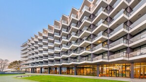A modern multi-story building with a unique geometric facade, featuring balconies with glass railings. - Apartamenty Sun & Snow Seaside Kołobrzeg (Kolobrzeg)