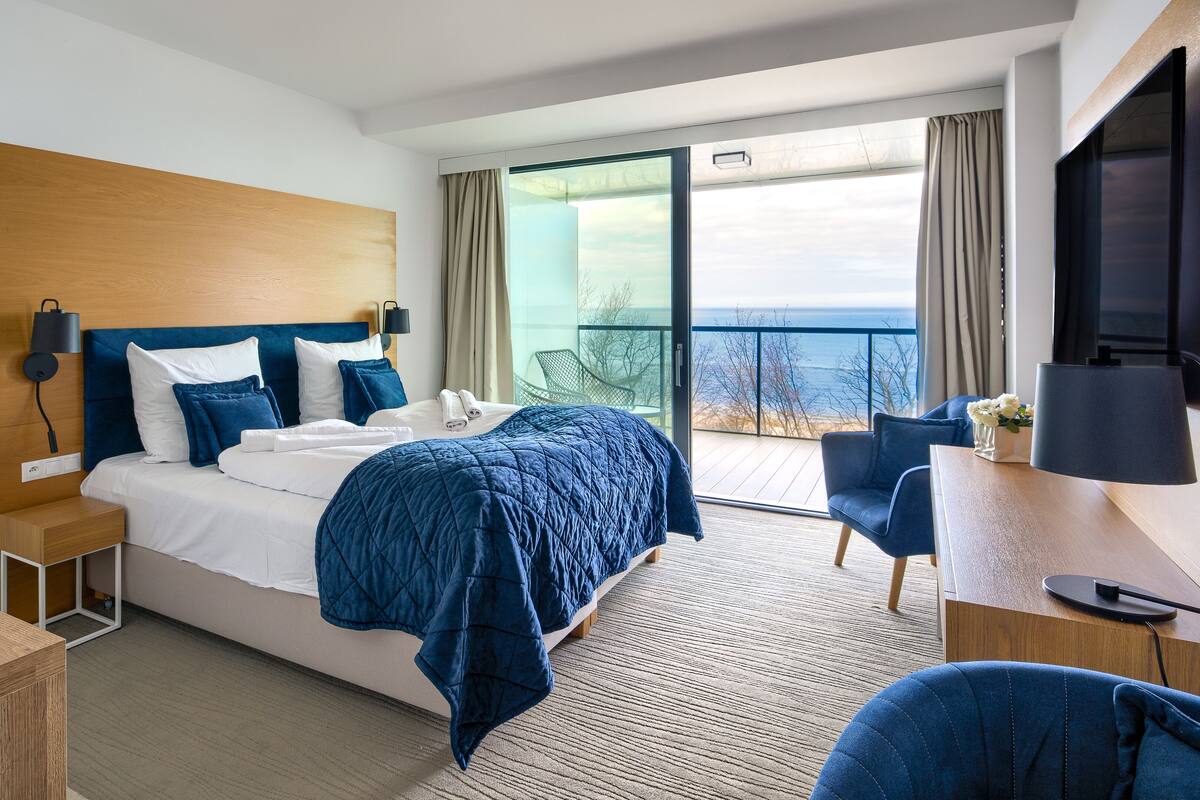 A modern hotel room with a large bed, a desk, a chair, and a TV.
