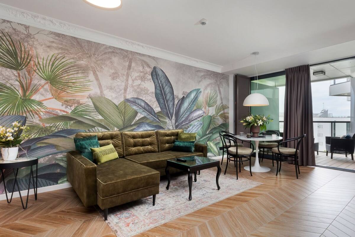 A modern living room with a large sectional sofa, a dining area with a round table, and a large window with curtains.
