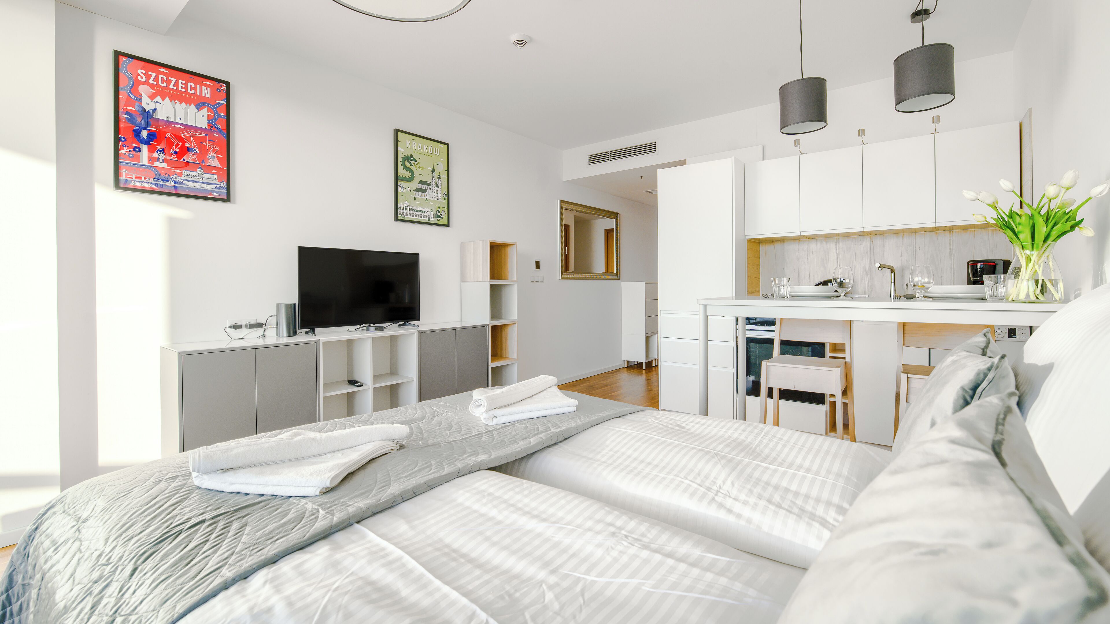 Une chambre d’hôtel moderne équipée d’un lit, d’une télévision, d’une kitchenette et d’une salle de bain, le tout visible à travers une porte ouverte.