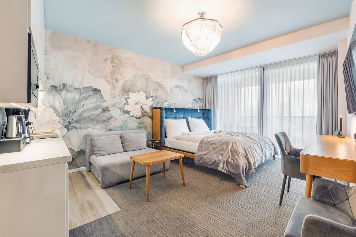 A modern hotel room with a bed, sofa, desk, and a large window.