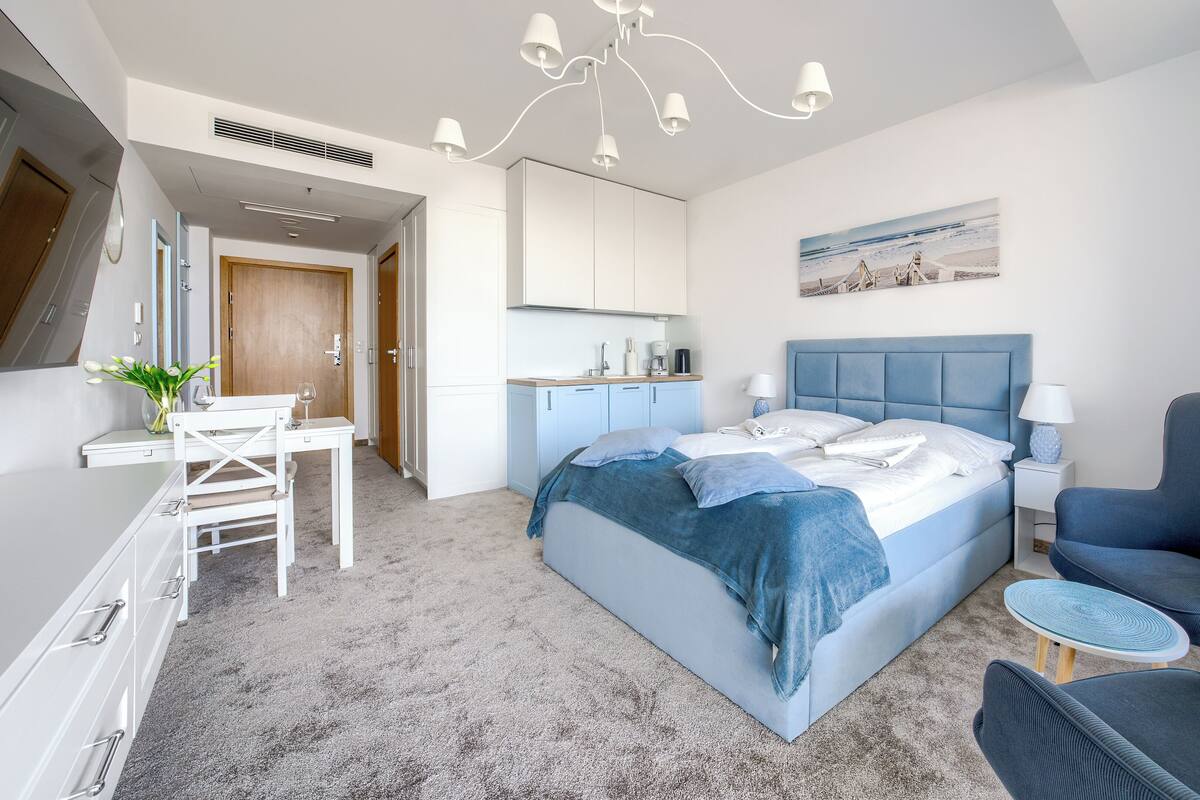 A modern hotel room with a bed, a desk, a chair, and a small table.