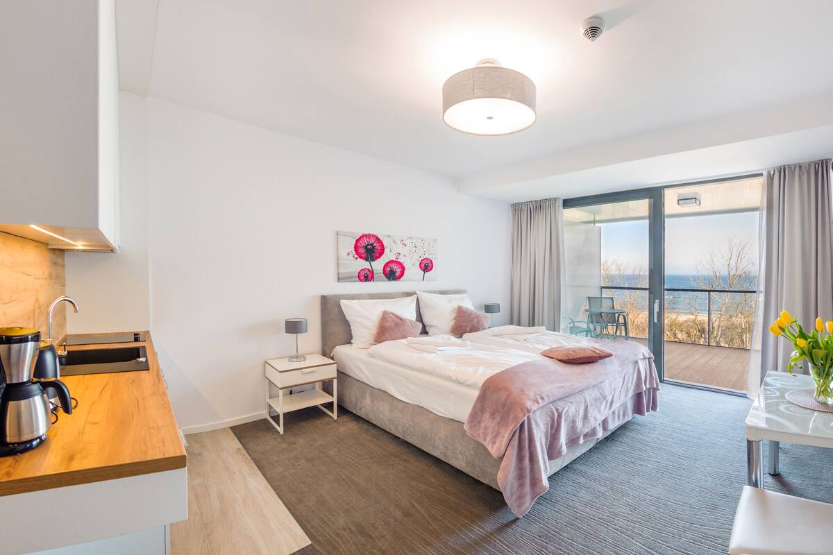 A modern hotel room with a bed, bedside table, and a view of the sea.