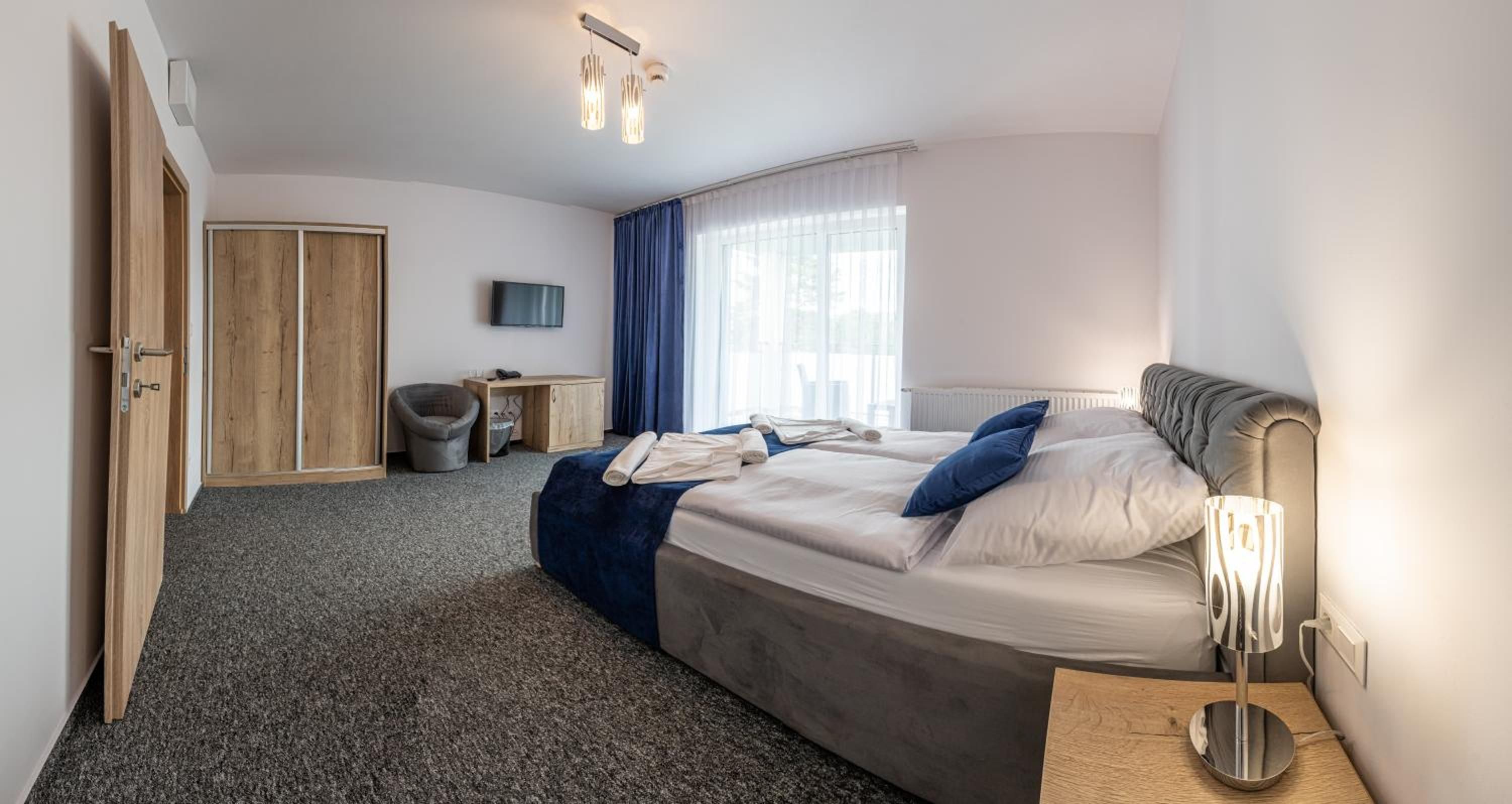 Quarto de hotel com cama, escrivaninha, cadeira, guarda-roupa e televisão.