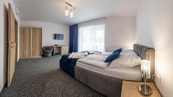 Quarto de hotel com cama, escrivaninha, cadeira, guarda-roupa e televisão.