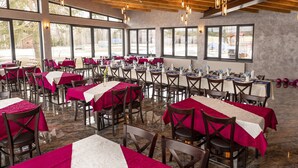 A restaurant with multiple tables covered in red and white tablecloths, wooden chairs, and hanging pendant lights. - Hotel Prístav (Trstená)