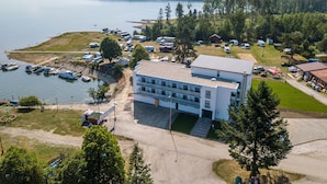 A modern building with a flat roof, surrounded by a parking area and a body of water. - Hotel Prístav (Trstená)