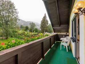 A balcony with a wooden railing, a small table with chairs, and a view of a garden with various plants and flowers. - Apartment Sankt Michael Near Ski Lift (Sankt Michael im Lungau)