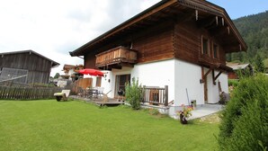 A wooden house with a balcony, a fenced yard, and a red umbrella.