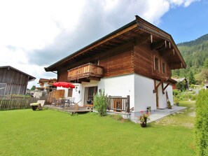 Ein zweistöckiges Holzhaus mit Balkon, rotem Sonnenschirm und gepflegtem Rasen.