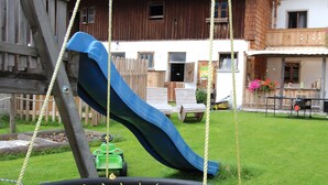 A swing set with a netted swing and a slide in a backyard.