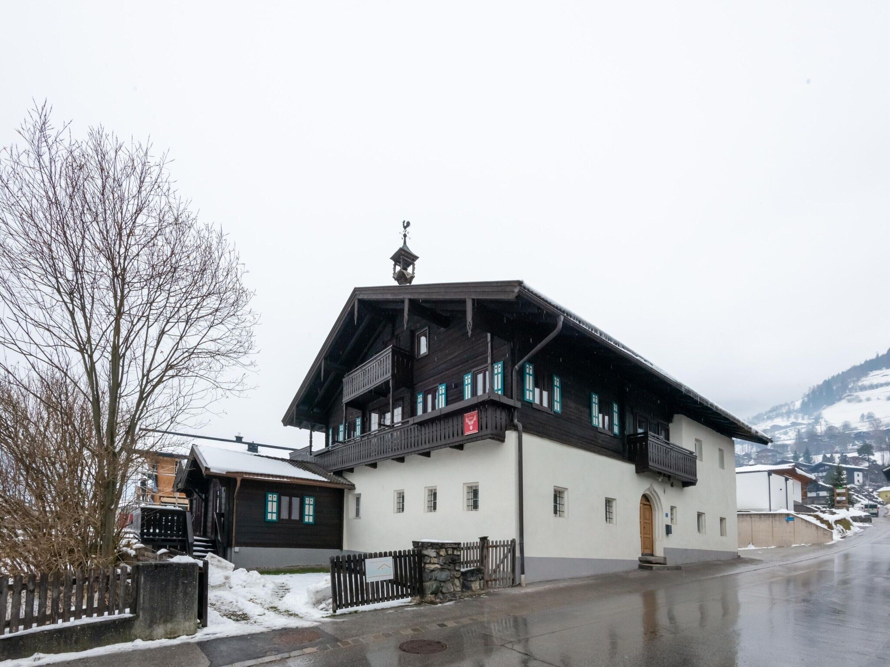 En traditionel træbygning med balkon, stenvæg og snedækket grund.