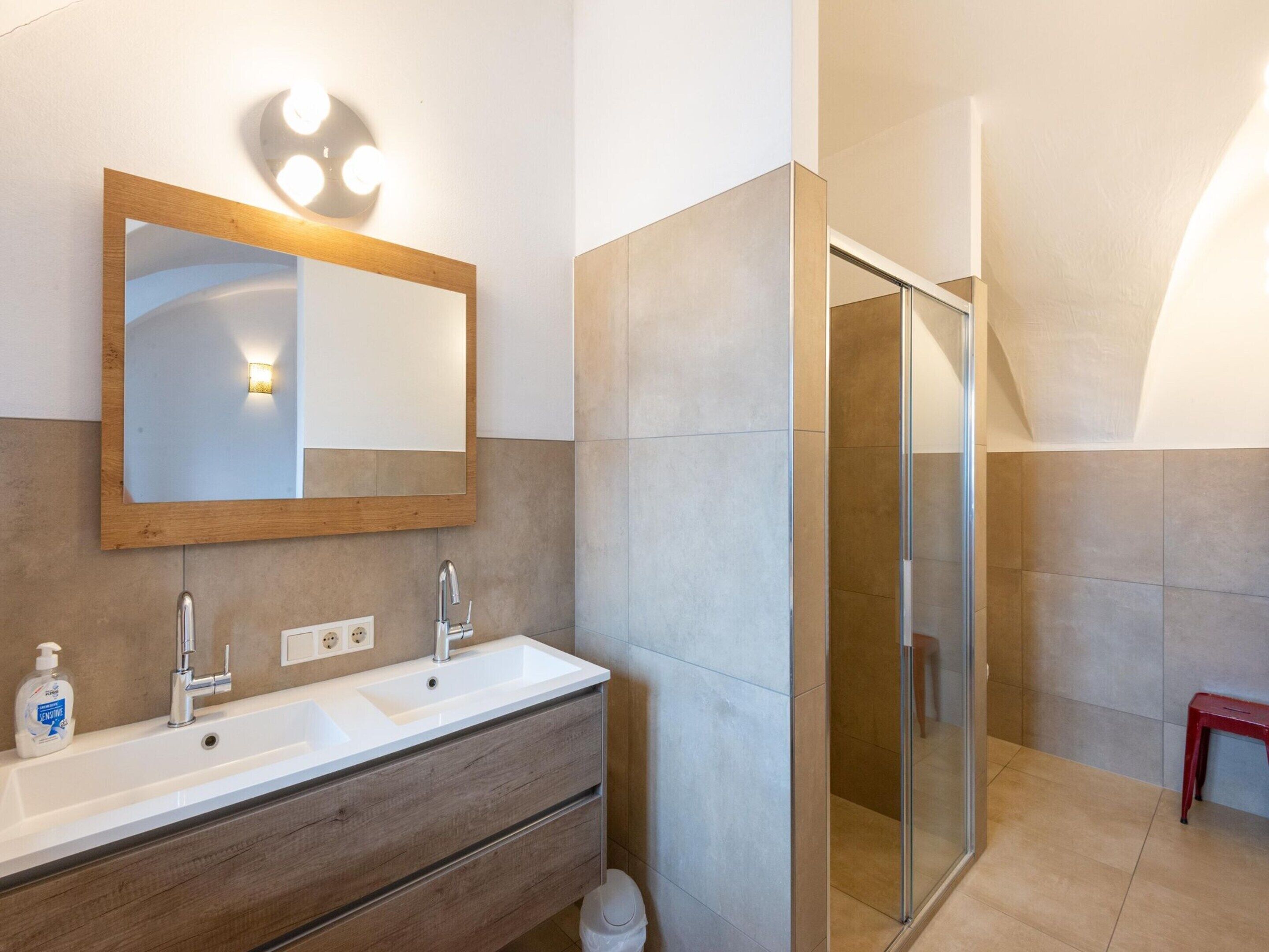 Un bagno moderno con un mobile bagno in legno, due lavabi, uno specchio grande e un box doccia in vetro.