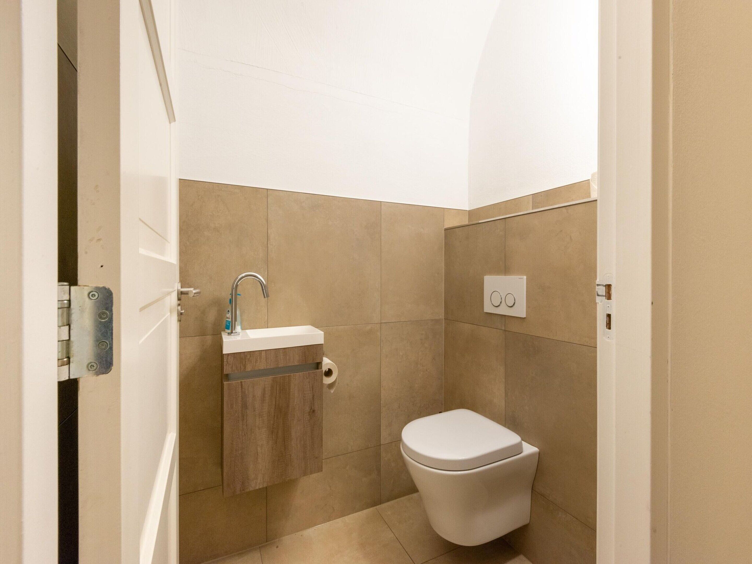 A small, modern bathroom with a toilet, a sink with a faucet, and a toilet paper holder.