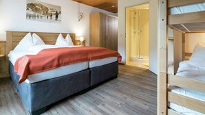 Une chambre d’hôtel avec un plafond en bois, un grand lit recouvert d’une couverture rouge, un lit superposé, une douche et une armoire en bois.