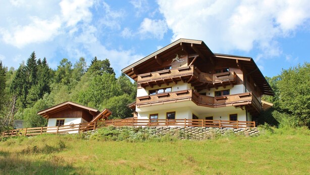 Un chalet à deux étages doté d’un balcon en bois et d’un mur en pierre à l’avant.