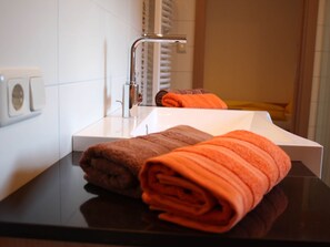 Et badeværelse med en hvid vask, en kromarmatur og to sammenrullede håndklæder, et brunt og et orange.
