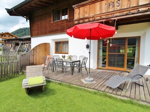 Et træhus med en patio, møbler, et rødt parasol og en træterrasse.