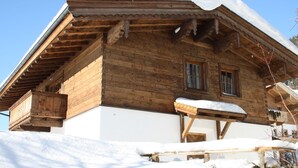 A wooden chalet with a sloped roof covered in snow, wooden balconies, and a snow-covered ground.