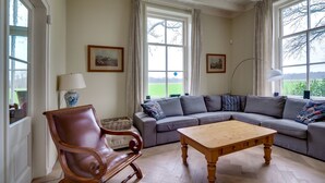 Ein Wohnzimmer mit einem Couchtisch aus Holz, einem Ledersessel, einem grauen Sofa mit gemusterten Kissen und zwei gerahmten Bildern an der Wand.