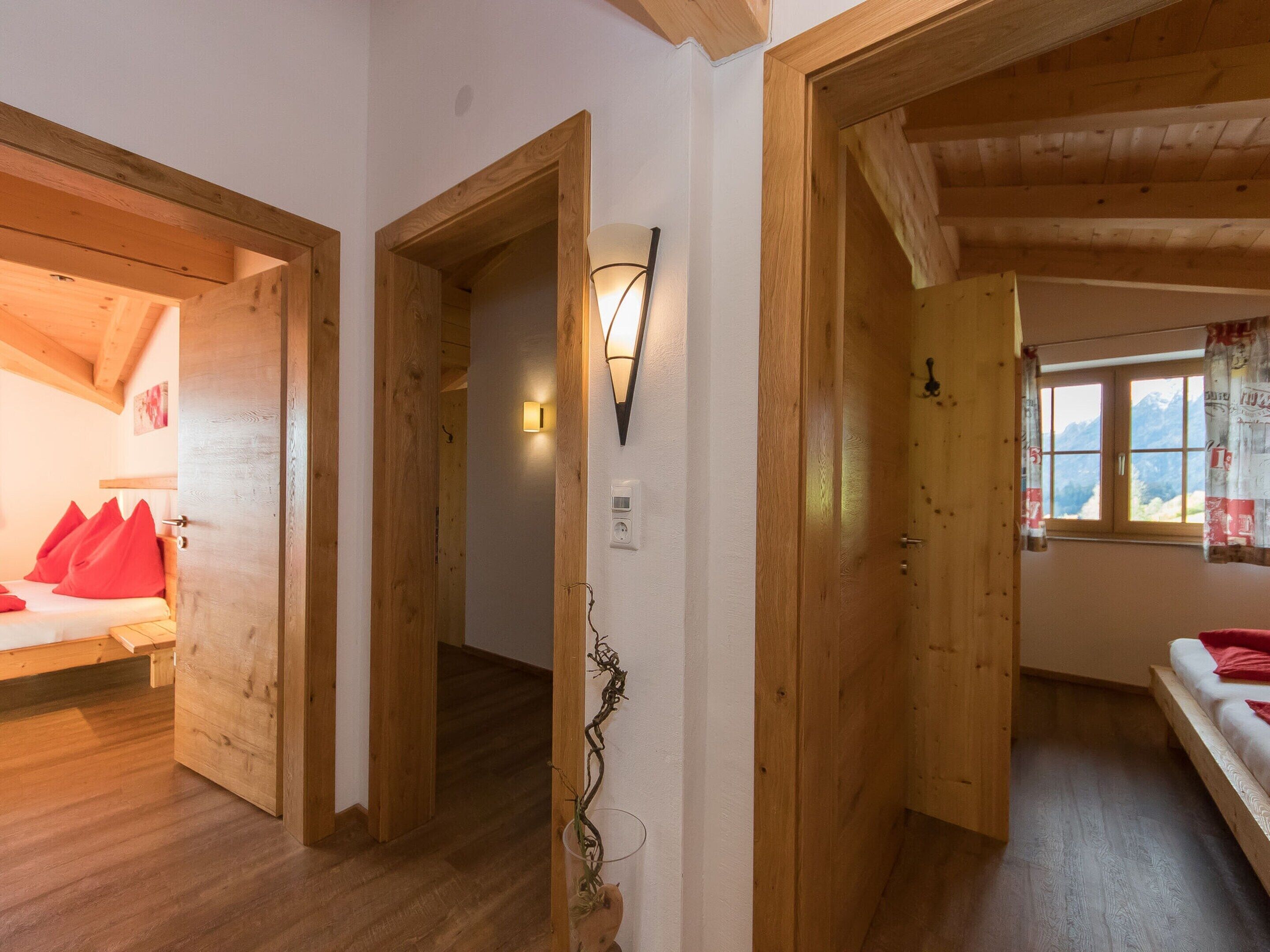 A wooden interior with a bed, a wall-mounted light, and a window with curtains.