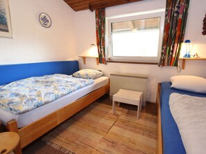 A bedroom with two beds, a small table, a radiator, and a window with curtains. - Spacious Chalet in Niedernsill near Skiing (Niedernsill)