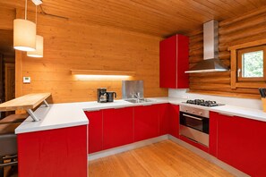 A compact kitchen with red cabinets, a stainless steel sink, a coffee maker, and a gas stove. - Rustic Chalet Near Skiwelt Wilder Kaiser (Woergl)