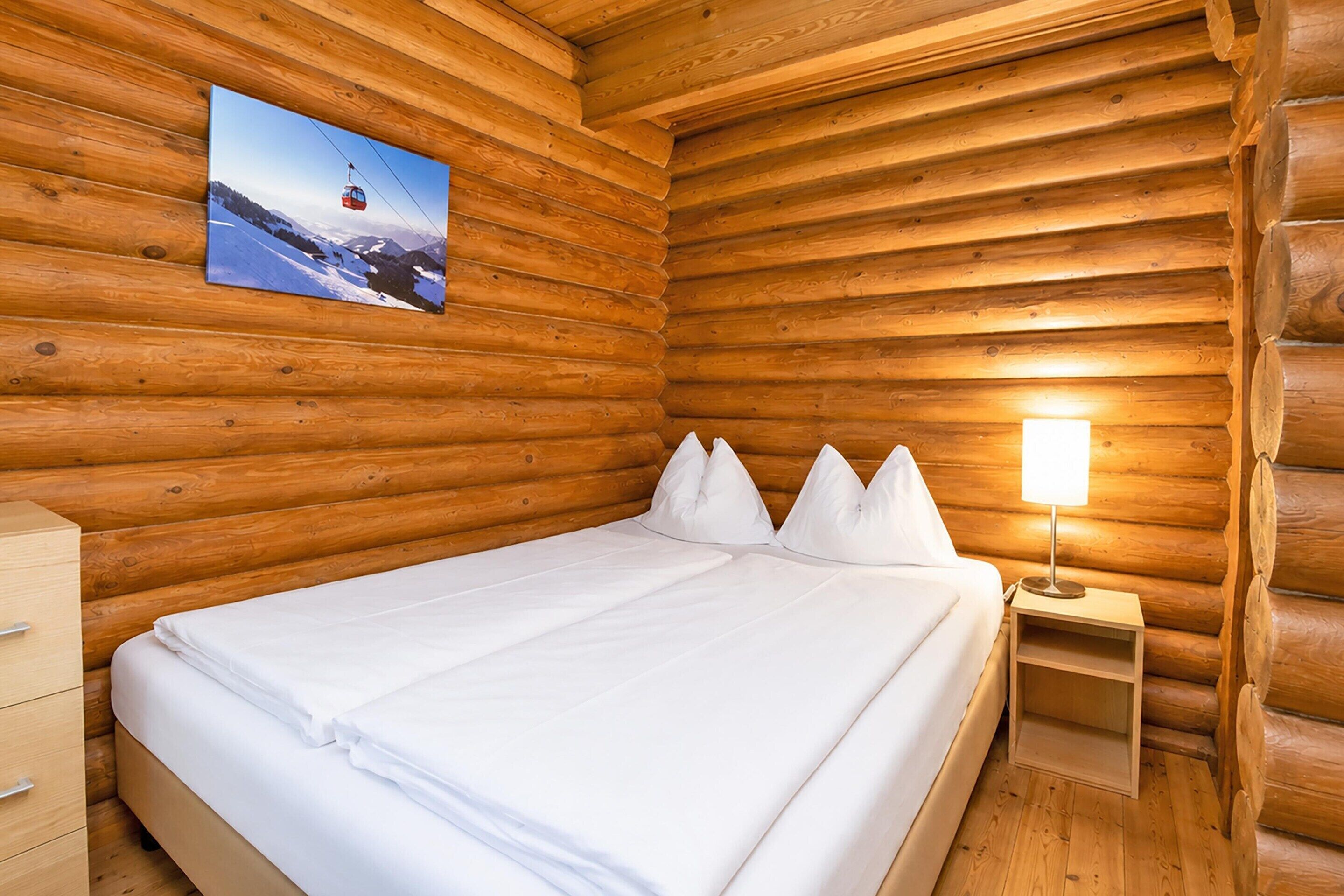 A wooden cabin room with a bed, pillows, a nightstand, and a lamp.