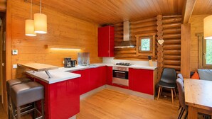 A modern kitchen with red cabinetry, a central island, and a dining area with a table and chairs. - Rustic Chalet Near Skiwelt Wilder Kaiser (Woergl)